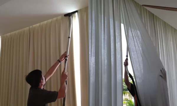 A man dusting and vacuuming curtains